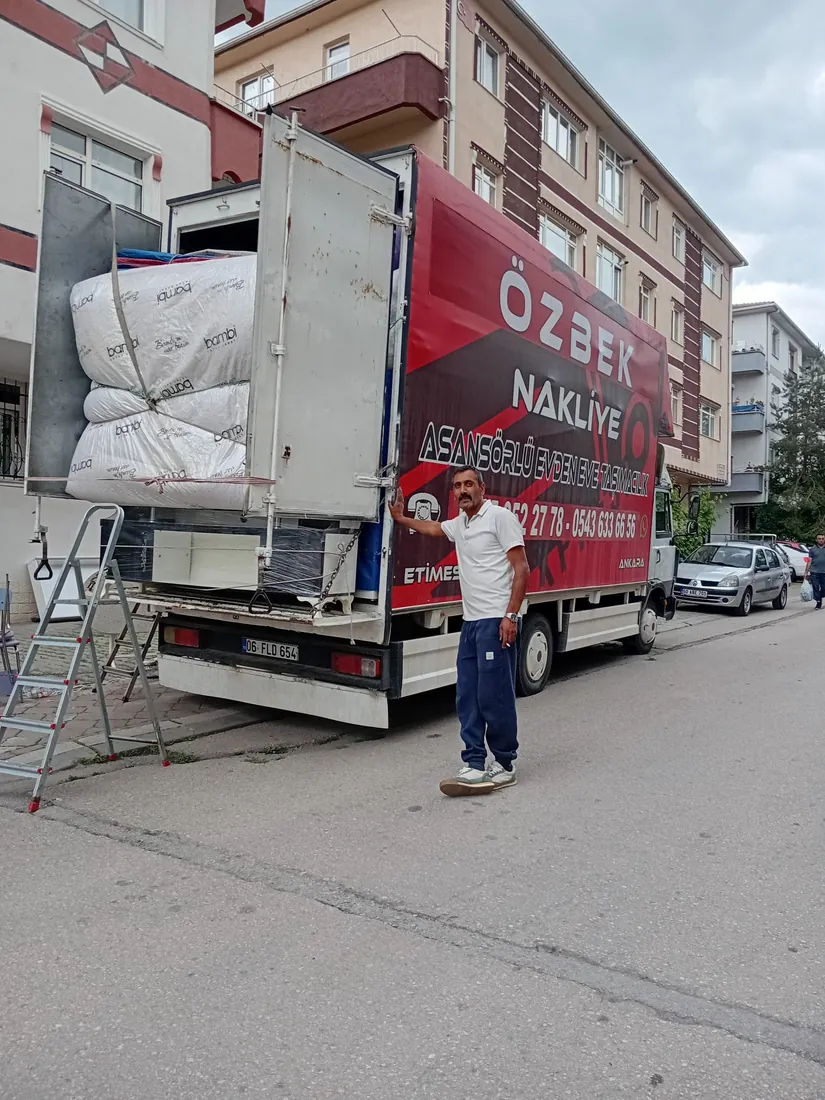 Paketlenmiş eşyalarla yüklenen Özbek Nakliyat aracı ve çalışanı